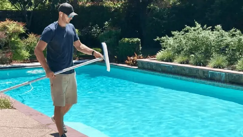 Summit Pool technician with handled brush working on a customer's pool.